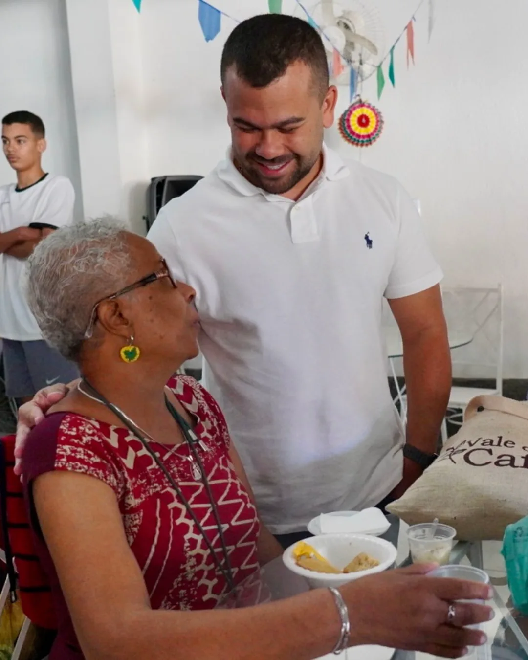Felipe Pampolha com a mão no ombro de uma senhora durante uma festa de bairro.