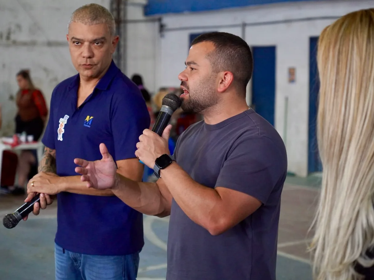 Felipe Pampolha falando ao microfone em um ginásio, ao lado de um apoiador.