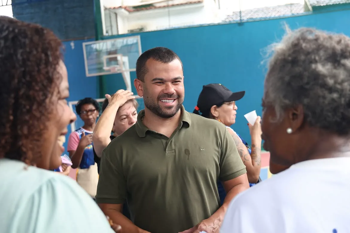 Felipe Pampolha sorrindo e cumprimentando moradoras em uma quadra poliesportiva.