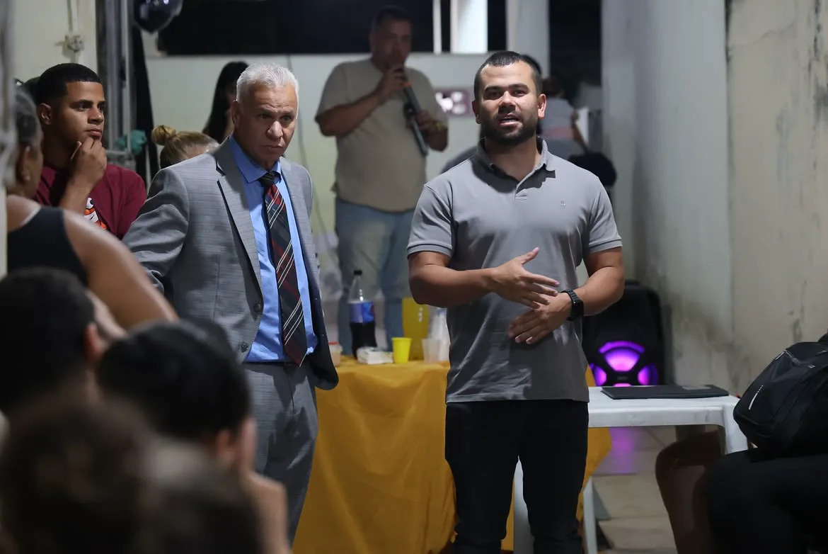 Felipe Pampolha falando em uma reunião comunitária à noite.